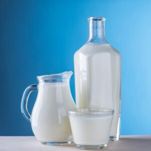 Minimalist still life of fresh milk in glassware against a blue background.