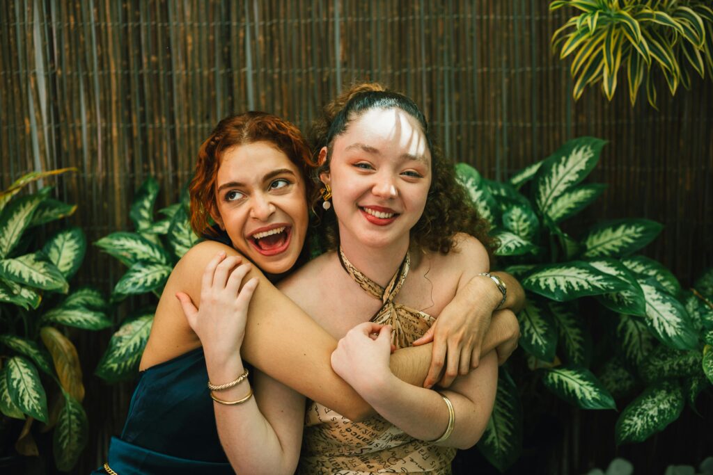 Two young adult women embracing and smiling joyfully against a lush garden backdrop.