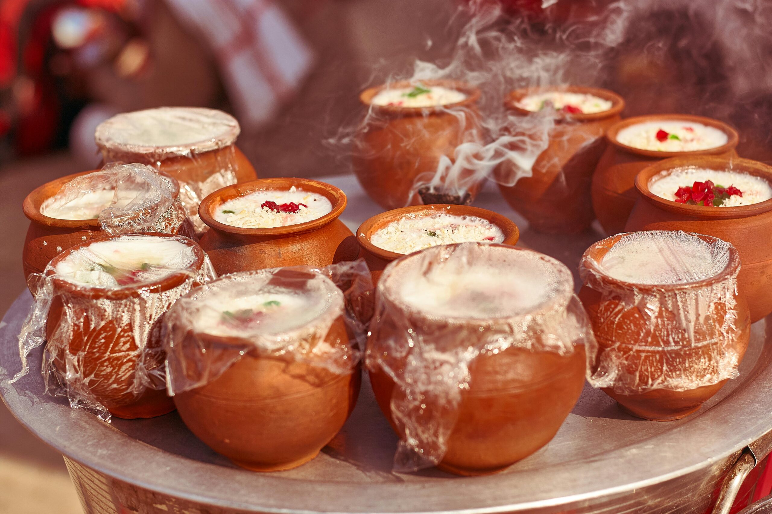 Steaming clay pots of traditional Indian lassi with vibrant garnishes.